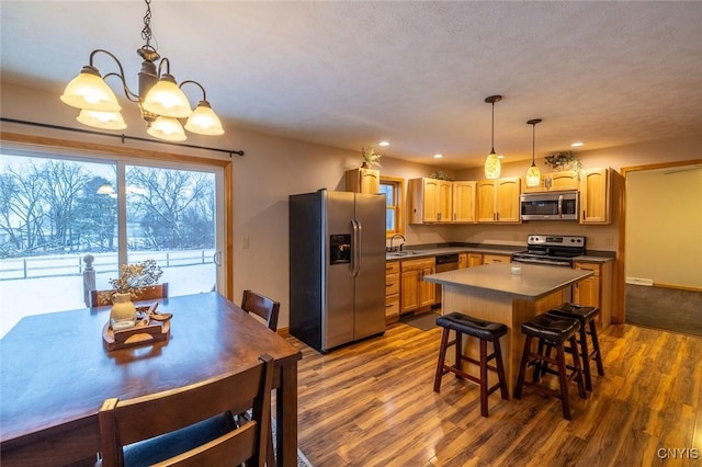 kitchen featuring dark wood-type flooring, a kitchen breakfast bar, a chandelier, decorative light fixtures, and appliances with stainless steel finishes