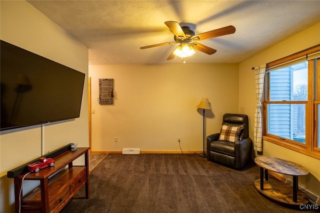 sitting room featuring dark colored carpet, ceiling fan, and a textured ceiling