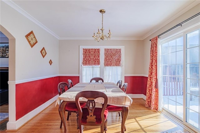 dining area with light hardwood / wood-style floors, ornamental molding, and an inviting chandelier