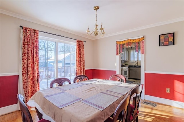 dining area featuring crown molding, light hardwood / wood-style flooring, sink, and a notable chandelier