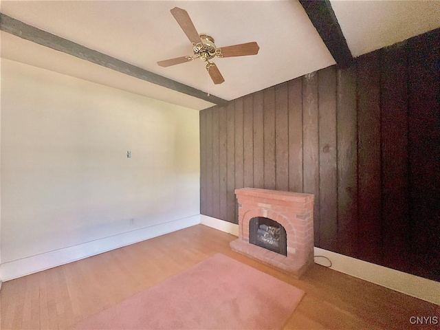 unfurnished living room featuring ceiling fan, a brick fireplace, beamed ceiling, wood walls, and light wood-type flooring