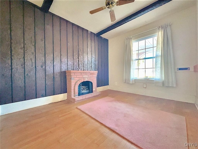 unfurnished living room featuring beamed ceiling, ceiling fan, a fireplace, and hardwood / wood-style flooring