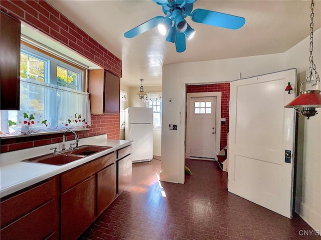 kitchen with sink, hanging light fixtures, brick wall, white fridge, and ceiling fan with notable chandelier