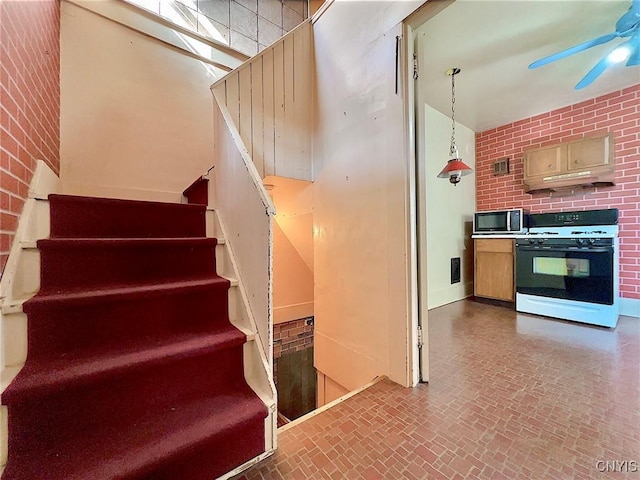 stairs with ceiling fan, a high ceiling, and brick wall