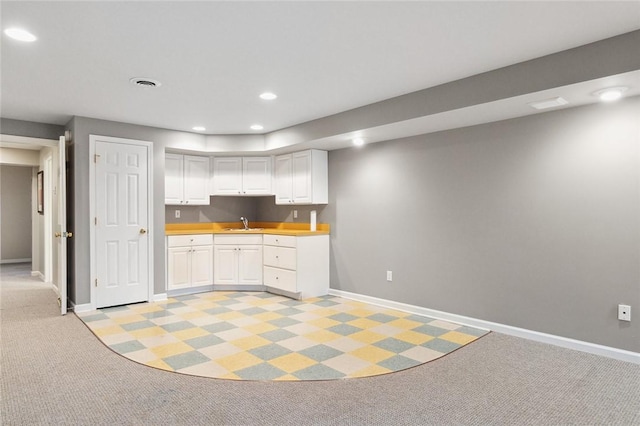 kitchen with white cabinets, light carpet, and sink