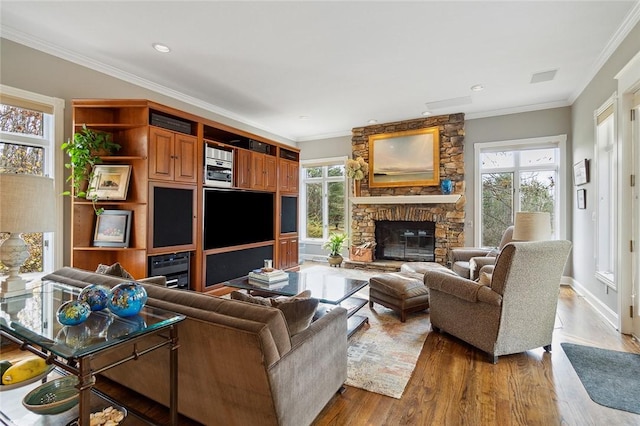 living room featuring a healthy amount of sunlight, a stone fireplace, crown molding, and hardwood / wood-style floors