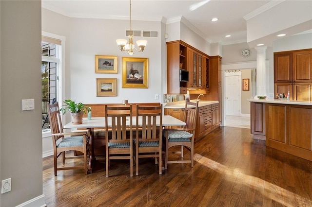 dining area with a notable chandelier, sink, ornamental molding, and dark wood-type flooring