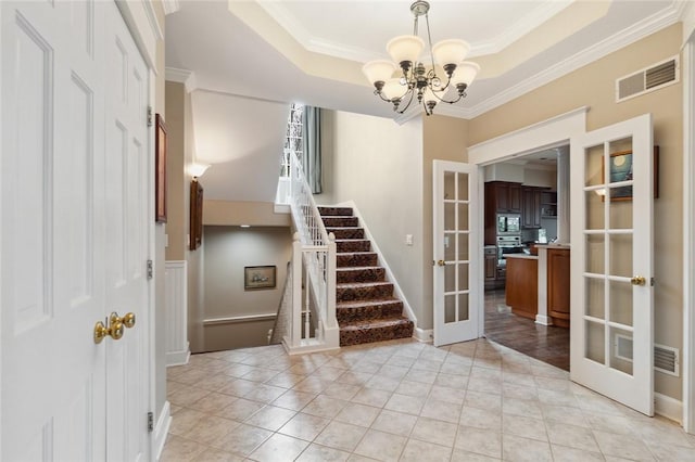 interior space with an inviting chandelier, french doors, ornamental molding, and a tray ceiling