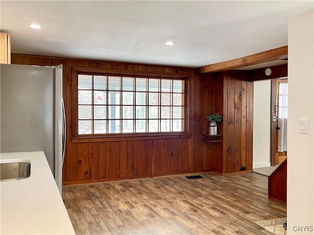 kitchen with stainless steel refrigerator, wooden walls, sink, and wood-type flooring