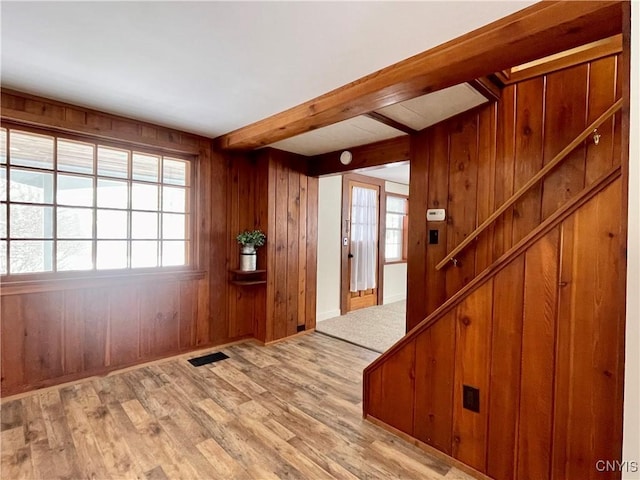 entrance foyer with wood walls, beamed ceiling, and light wood-type flooring