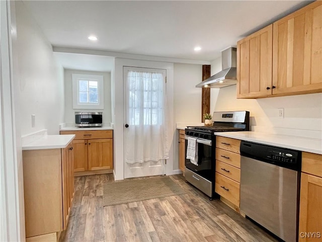 kitchen with wall chimney exhaust hood, light brown cabinets, stainless steel appliances, and light hardwood / wood-style flooring