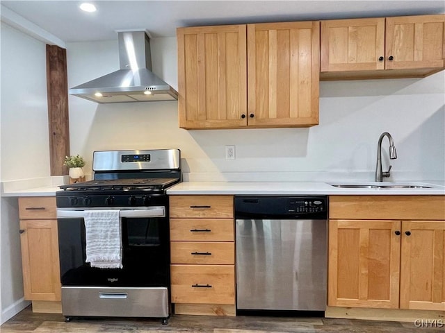 kitchen with wall chimney range hood, sink, light brown cabinetry, appliances with stainless steel finishes, and wood-type flooring