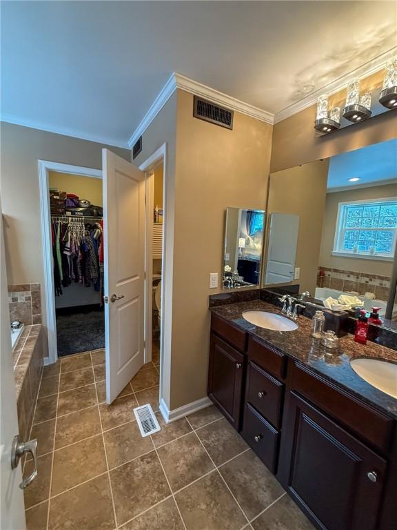 bathroom featuring tile patterned flooring, vanity, crown molding, and a washtub