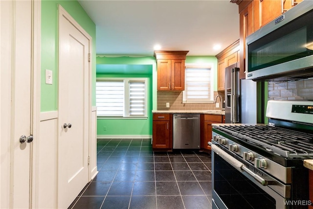 kitchen featuring appliances with stainless steel finishes, tasteful backsplash, light stone counters, dark tile patterned floors, and sink