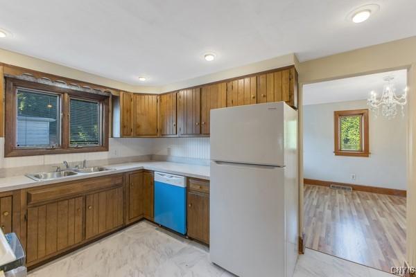 kitchen with pendant lighting, dishwasher, white refrigerator, sink, and a notable chandelier