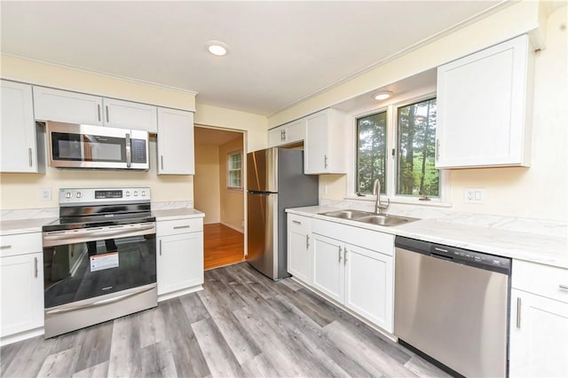 kitchen featuring light stone countertops, appliances with stainless steel finishes, sink, light hardwood / wood-style flooring, and white cabinets