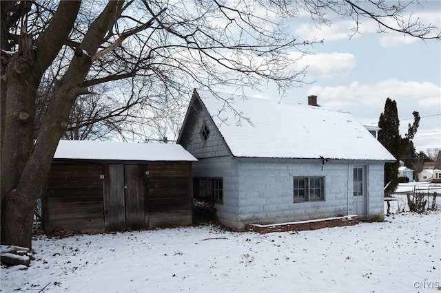 snow covered rear of property featuring an outdoor structure