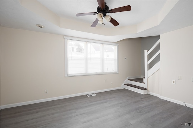 unfurnished living room featuring a raised ceiling, ceiling fan, and hardwood / wood-style flooring