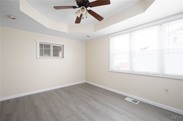 unfurnished room with a raised ceiling, ceiling fan, and light wood-type flooring