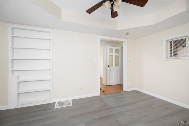 empty room with ceiling fan, wood-type flooring, and a tray ceiling