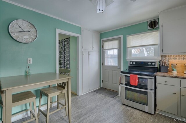 kitchen with light wood-type flooring, backsplash, crown molding, white cabinetry, and stainless steel electric range