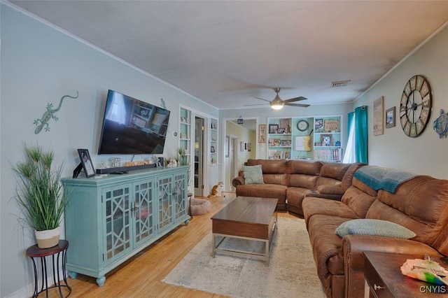 living room featuring built in shelves, ceiling fan, crown molding, and light hardwood / wood-style flooring