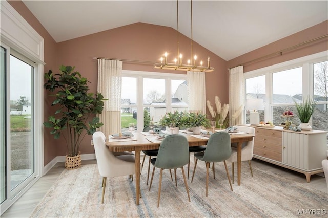 dining room featuring a notable chandelier, a healthy amount of sunlight, vaulted ceiling, and light hardwood / wood-style flooring