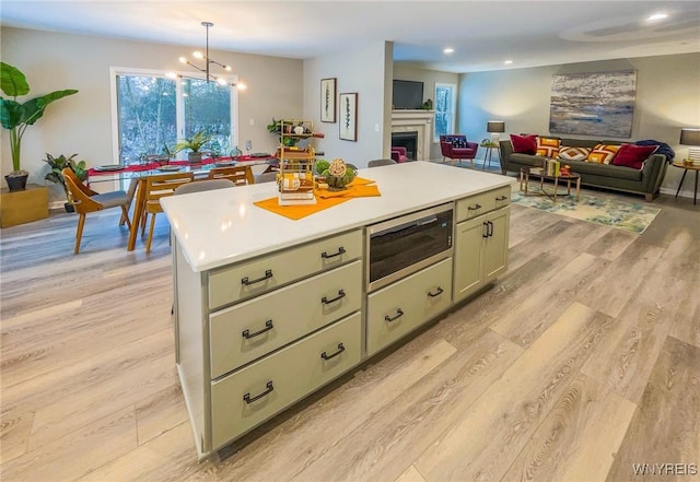 kitchen featuring light wood-type flooring, built in microwave, decorative light fixtures, a notable chandelier, and a kitchen island