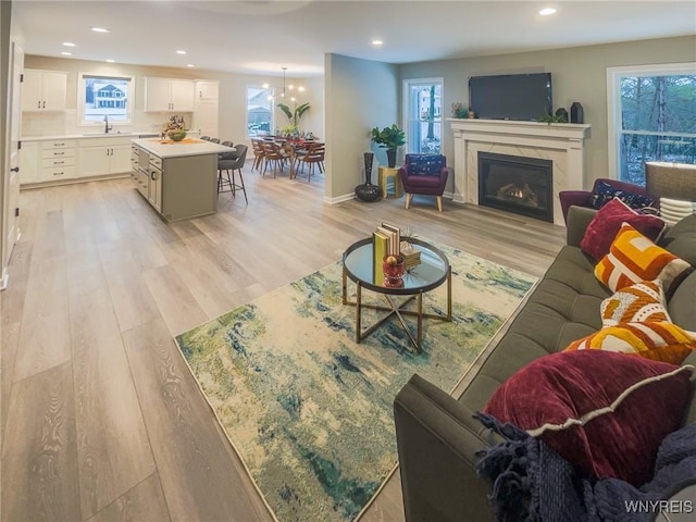 living room featuring a healthy amount of sunlight, a premium fireplace, sink, and light hardwood / wood-style flooring