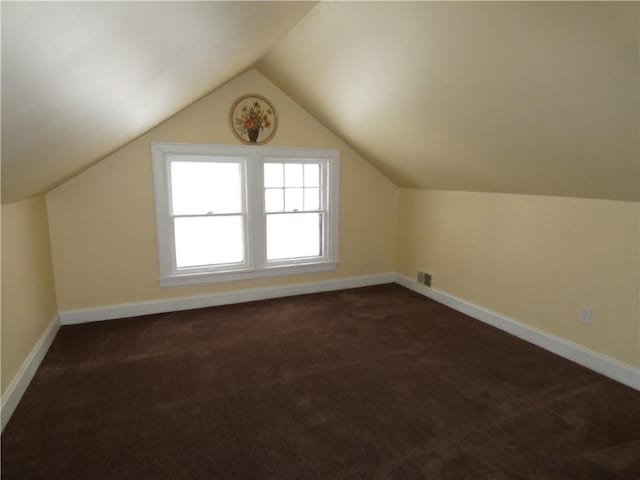 bonus room with dark colored carpet and lofted ceiling