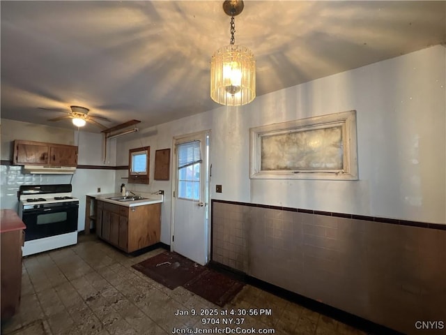 kitchen featuring white gas range, ceiling fan, sink, tile walls, and hanging light fixtures