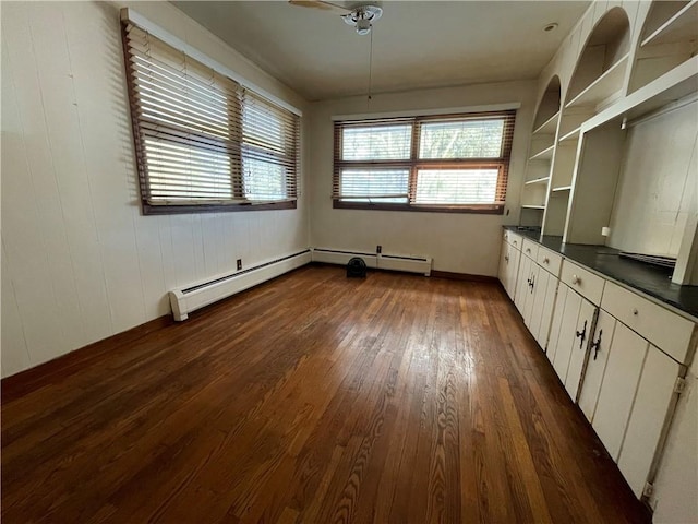 interior space with built in shelves, dark hardwood / wood-style floors, baseboard heating, and ceiling fan