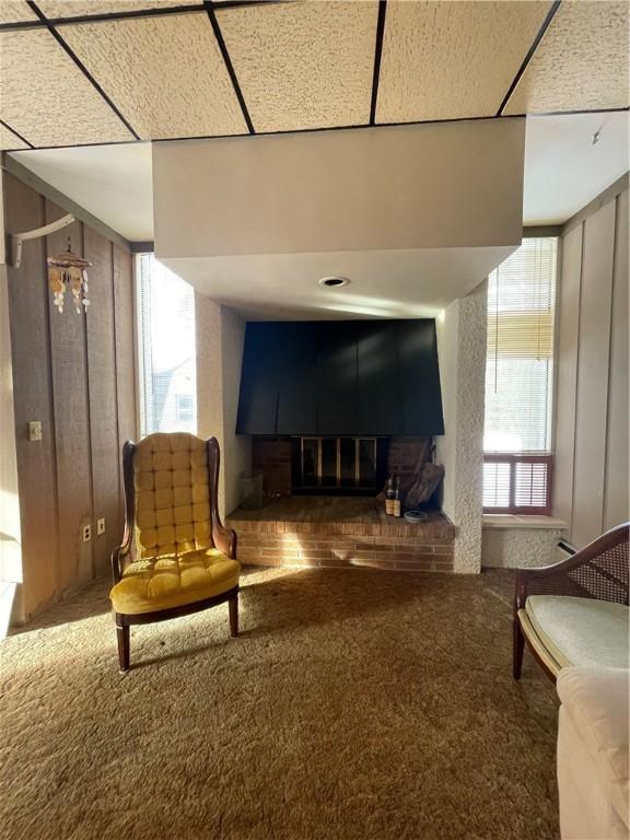 living area with carpet flooring, wooden walls, and a brick fireplace