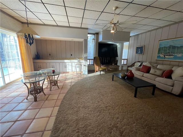 tiled living room featuring ceiling fan, wood walls, and a drop ceiling