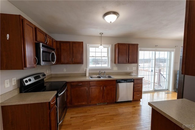 kitchen with stainless steel appliances, light hardwood / wood-style flooring, hanging light fixtures, and sink