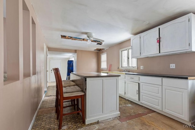 kitchen with ceiling fan, sink, a kitchen island, a breakfast bar, and white cabinets