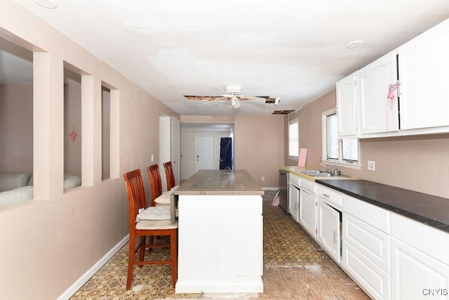 kitchen featuring white cabinetry, ceiling fan, a center island, sink, and a breakfast bar