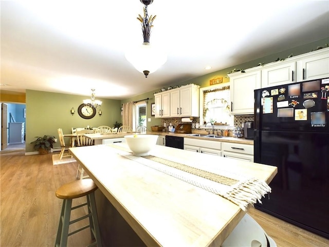 kitchen featuring hanging light fixtures, white cabinets, black appliances, and tasteful backsplash