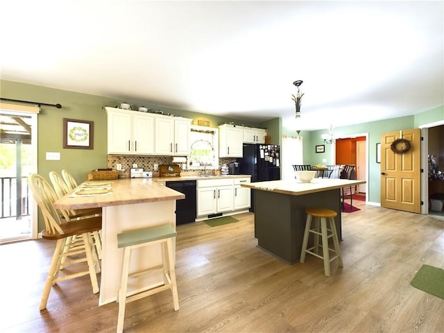 kitchen with white cabinetry, a breakfast bar area, backsplash, pendant lighting, and black appliances