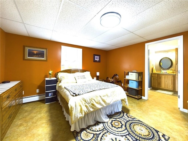 bedroom with a drop ceiling, a baseboard heating unit, and connected bathroom