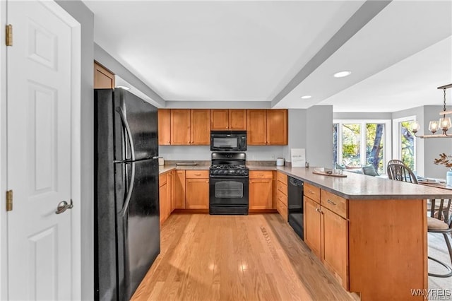 kitchen featuring a notable chandelier, light wood finished floors, black appliances, a peninsula, and a kitchen bar