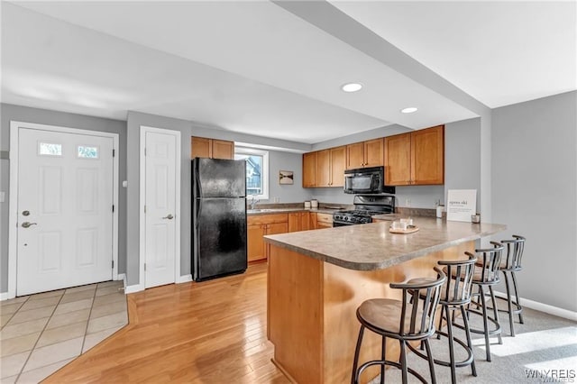 kitchen featuring baseboards, a breakfast bar, a peninsula, black appliances, and a sink