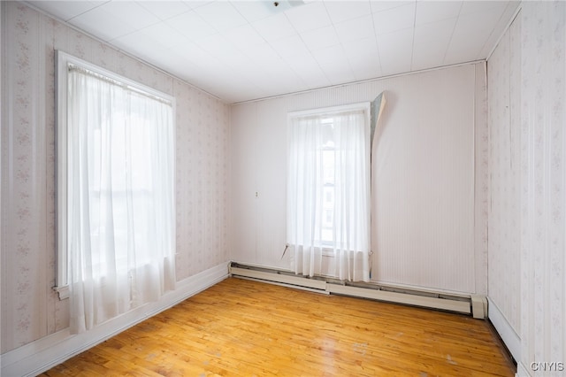 unfurnished room featuring hardwood / wood-style floors and a baseboard heating unit