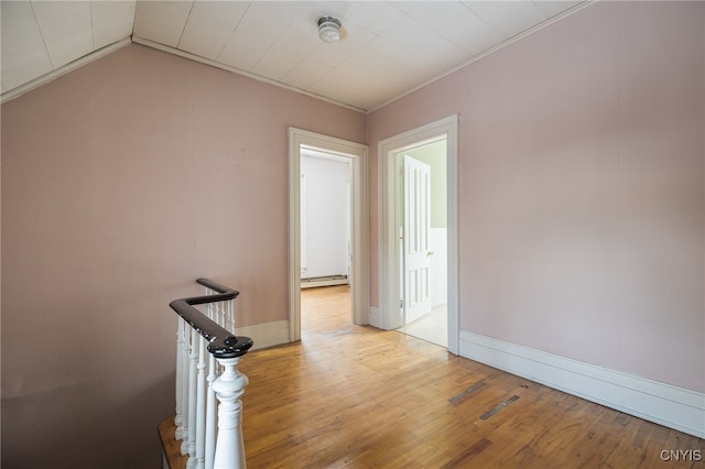 empty room featuring ornamental molding, a baseboard radiator, vaulted ceiling, and light wood-type flooring