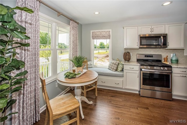 kitchen featuring white cabinetry, light stone counters, dark hardwood / wood-style flooring, stainless steel appliances, and decorative backsplash