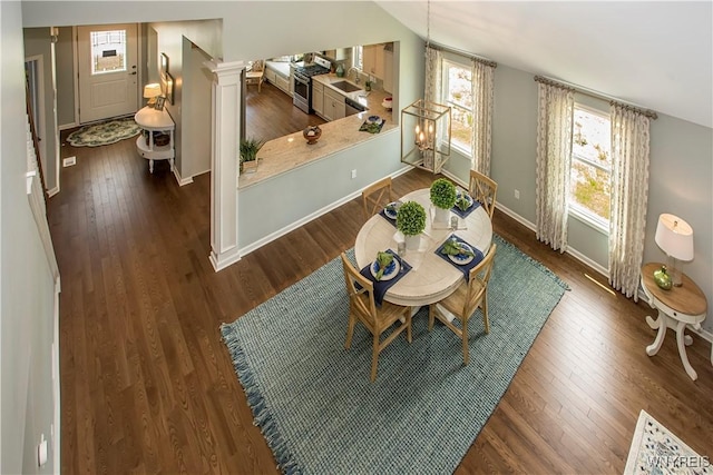 dining room with sink, an inviting chandelier, decorative columns, dark hardwood / wood-style flooring, and vaulted ceiling