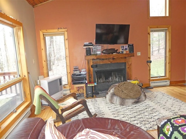 living room with lofted ceiling, baseboard heating, a healthy amount of sunlight, and hardwood / wood-style floors