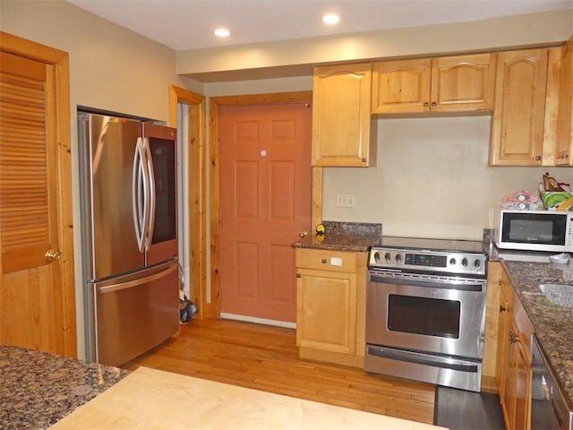 kitchen with light brown cabinets, appliances with stainless steel finishes, light hardwood / wood-style flooring, and dark stone countertops