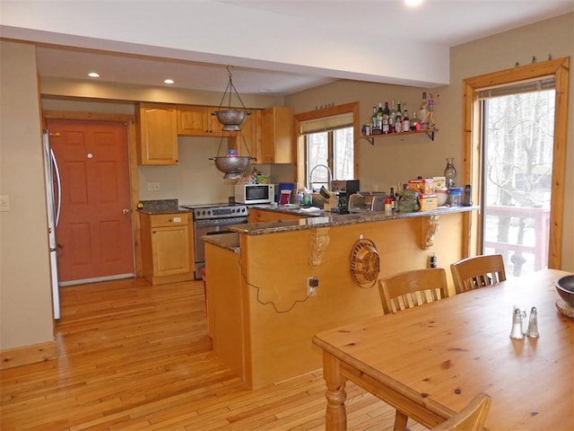 kitchen with appliances with stainless steel finishes, dark stone counters, sink, kitchen peninsula, and light hardwood / wood-style flooring