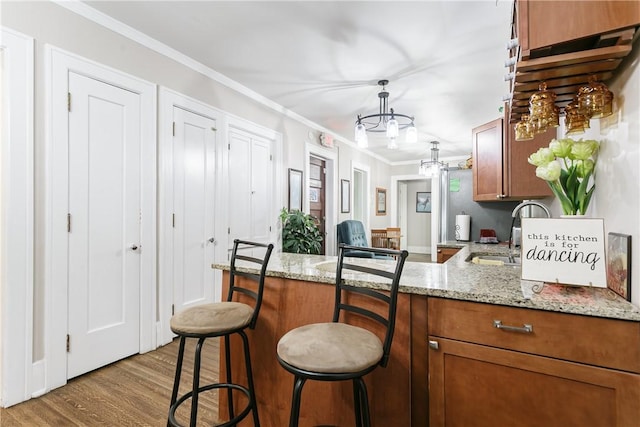 kitchen with kitchen peninsula, light wood-type flooring, ornamental molding, pendant lighting, and a breakfast bar area